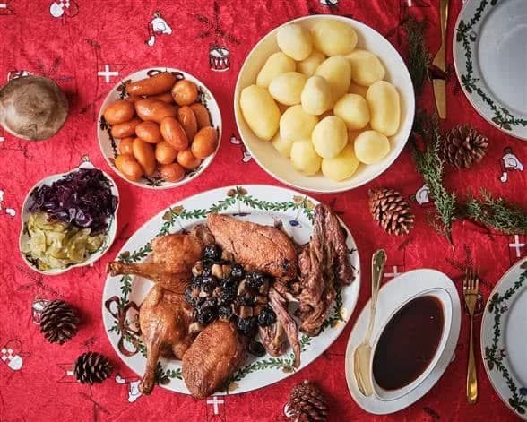 Flæskesteg med sprød svær på et skærebræt, med rødkål, grangrene og levende lys